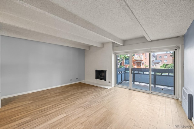 555 E 10th Ave Unit 111, Denver, CO 80203 - unfurnished living room with light wood finished floors, a textured ceiling, a fireplace, beam ceiling, and baseboards
