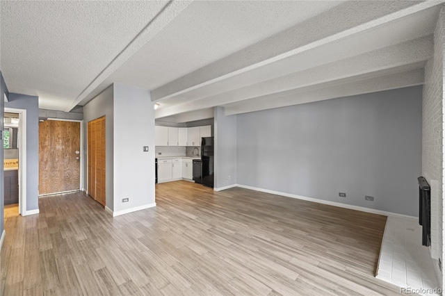 555 E 10th Ave Unit 111, Denver, CO 80203 - unfurnished living room featuring a textured ceiling, light wood-style flooring, baseboards, and a sink