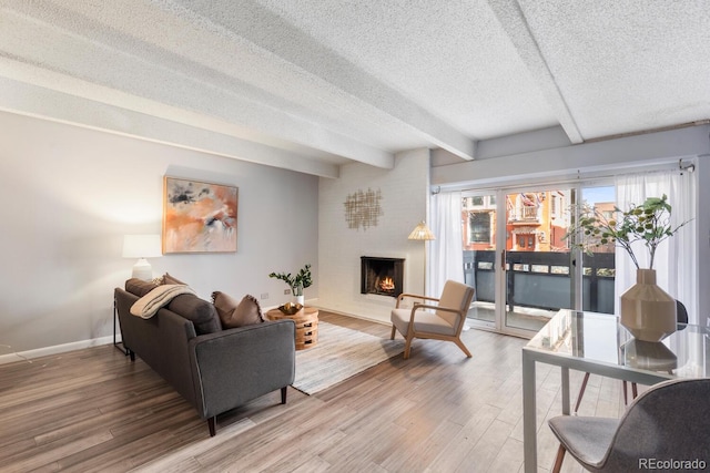 555 E 10th Ave Unit 111, Denver, CO 80203 - living room with beam ceiling, a textured ceiling, a large fireplace, wood finished floors, and baseboards