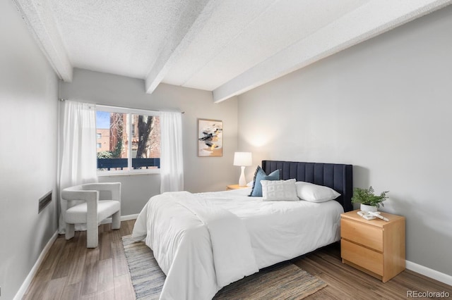 555 E 10th Ave Unit 111, Denver, CO 80203 - bedroom featuring beamed ceiling, a textured ceiling, wood finished floors, and baseboards