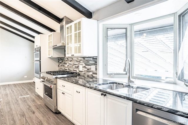 kitchen featuring appliances with stainless steel finishes, sink, dark stone countertops, white cabinets, and vaulted ceiling with beams