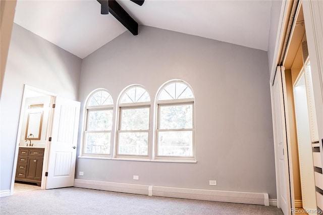 unfurnished bedroom featuring beam ceiling, ensuite bathroom, high vaulted ceiling, and light carpet