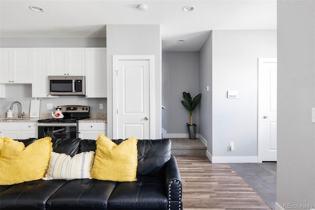 kitchen with stainless steel appliances, white cabinetry, sink, and light stone counters