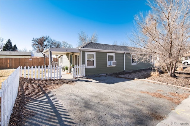 ranch-style home with driveway, a porch, fence, cooling unit, and roof with shingles