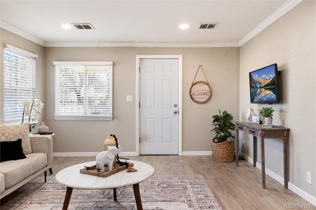 living area featuring visible vents, baseboards, light wood-style floors, and crown molding