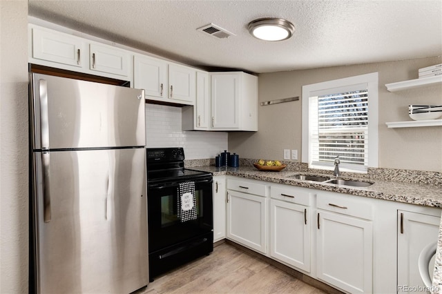 kitchen featuring visible vents, electric range, freestanding refrigerator, a sink, and white cabinetry