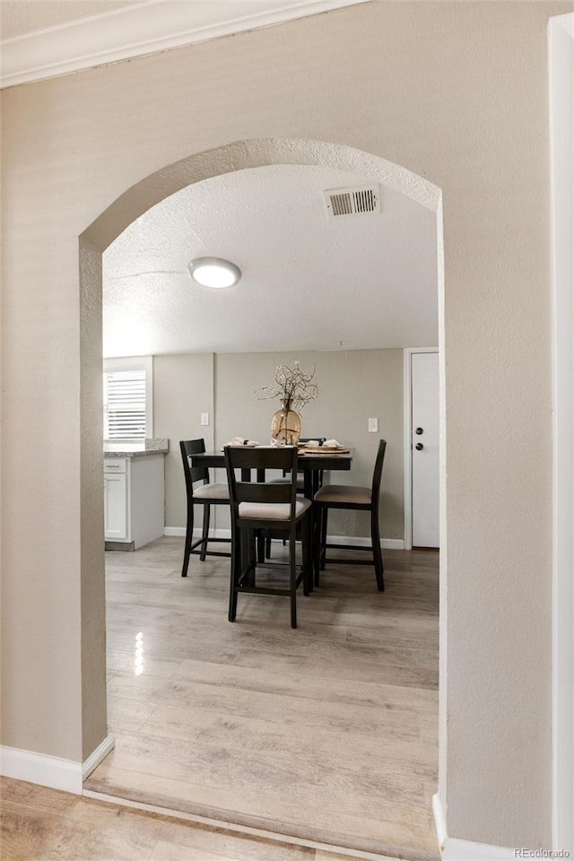 dining room with visible vents, arched walkways, light wood-style floors, and baseboards