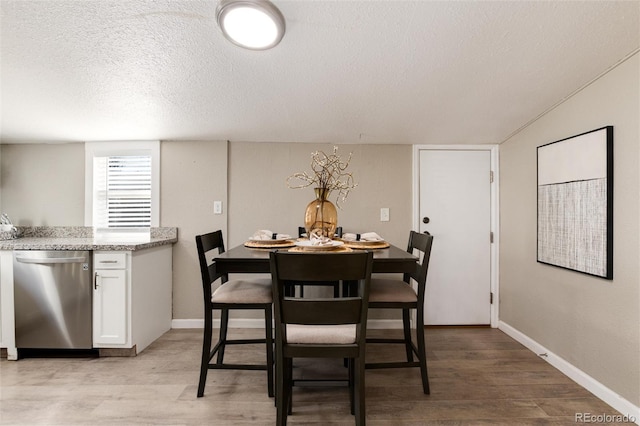 dining space with light wood finished floors, a textured ceiling, and baseboards