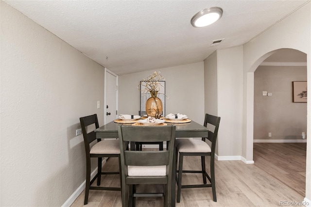 dining space with arched walkways, visible vents, light wood finished floors, and baseboards