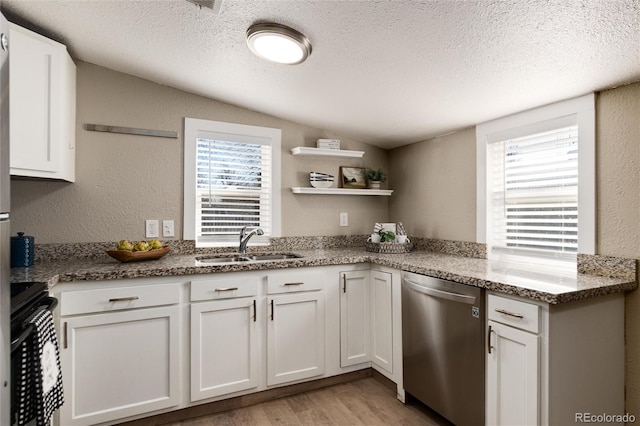 kitchen featuring a sink, stainless steel dishwasher, lofted ceiling, stove, and a textured wall