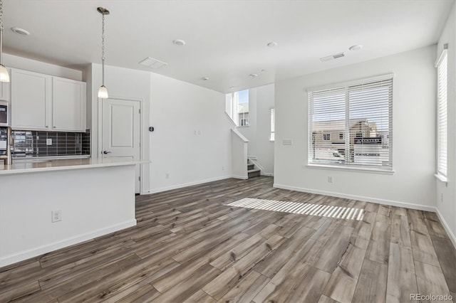 unfurnished living room with stairs, visible vents, baseboards, and wood finished floors