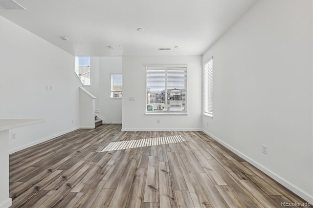 unfurnished living room with stairs, visible vents, baseboards, and wood finished floors