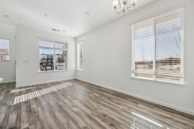 empty room featuring baseboards, a chandelier, and wood finished floors