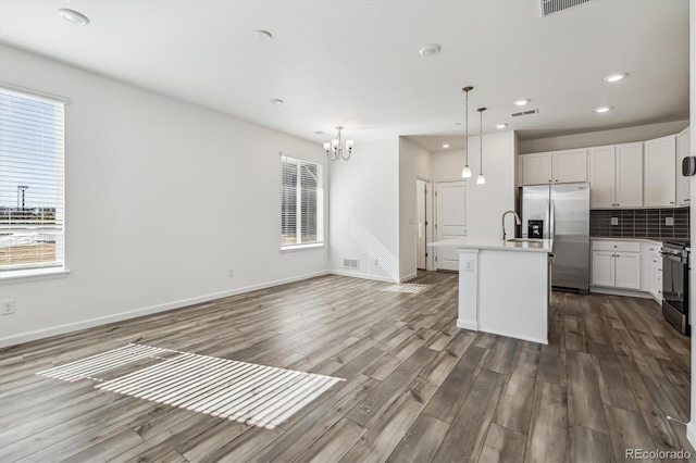 kitchen featuring dark wood finished floors, stainless steel appliances, tasteful backsplash, light countertops, and an island with sink