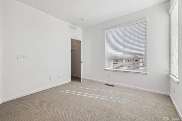 empty room with carpet, visible vents, and baseboards