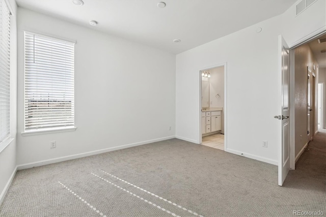 unfurnished bedroom featuring light carpet, ensuite bath, baseboards, and visible vents