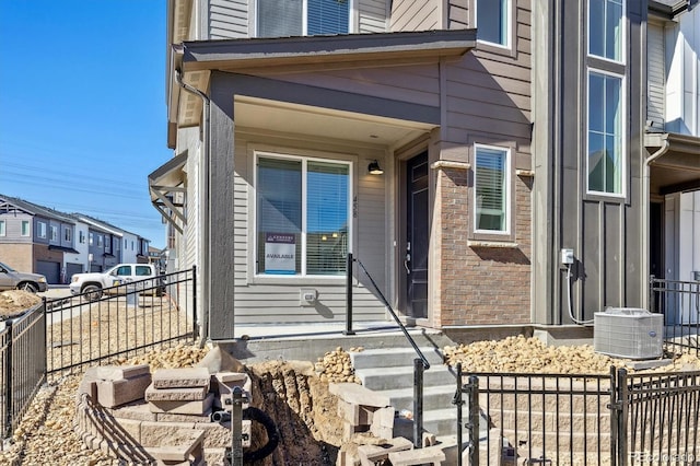 view of exterior entry with central AC, brick siding, and fence