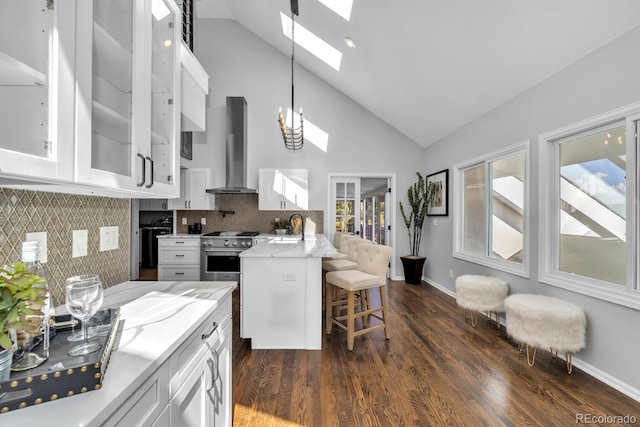 kitchen featuring wall chimney range hood, high end stainless steel range oven, backsplash, white cabinets, and decorative light fixtures