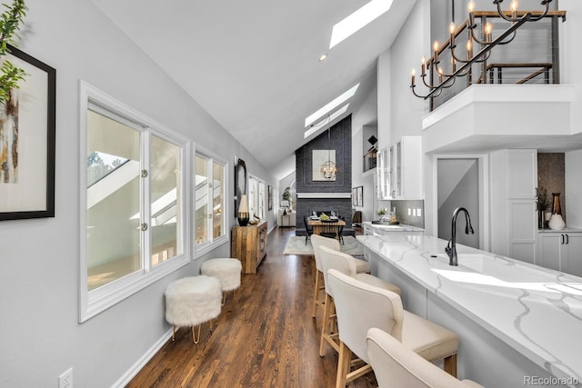 kitchen featuring a breakfast bar, a skylight, light stone countertops, white cabinets, and decorative light fixtures