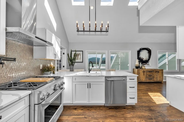 kitchen with sink, appliances with stainless steel finishes, white cabinetry, backsplash, and wall chimney exhaust hood