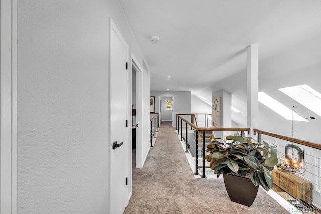 hall with vaulted ceiling with skylight and light carpet