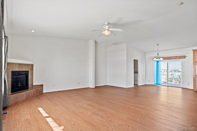 unfurnished living room featuring ceiling fan with notable chandelier, light hardwood / wood-style floors, and a tile fireplace