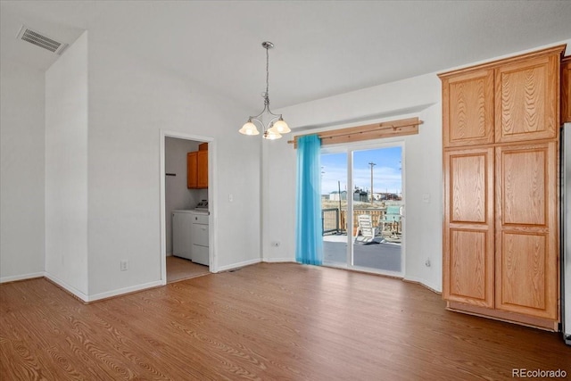 unfurnished dining area with an inviting chandelier, washer and clothes dryer, light hardwood / wood-style floors, and vaulted ceiling