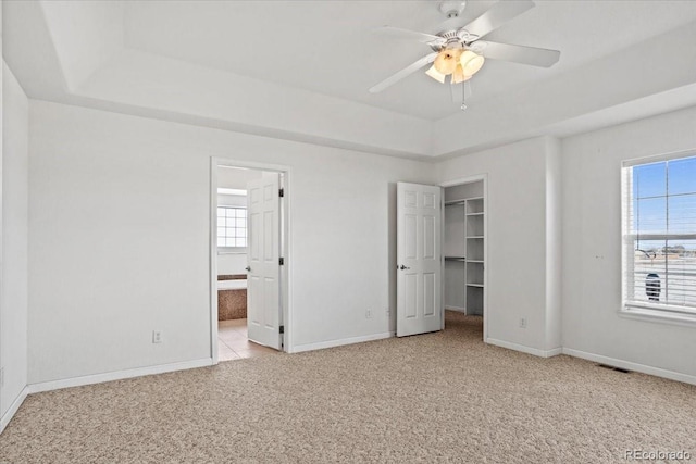 unfurnished bedroom with ensuite bathroom, a spacious closet, light colored carpet, a raised ceiling, and a closet