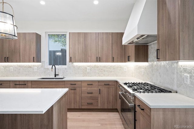 kitchen with sink, light hardwood / wood-style flooring, premium range hood, decorative light fixtures, and high end stainless steel range