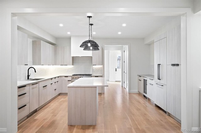 kitchen with pendant lighting, backsplash, sink, light hardwood / wood-style flooring, and a kitchen island