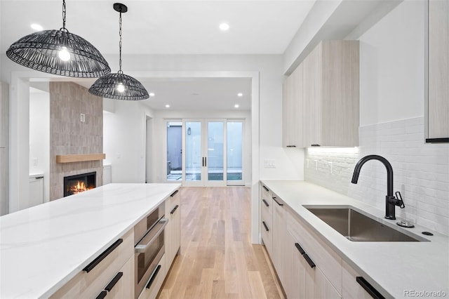 kitchen featuring sink, tasteful backsplash, light hardwood / wood-style flooring, decorative light fixtures, and a tiled fireplace