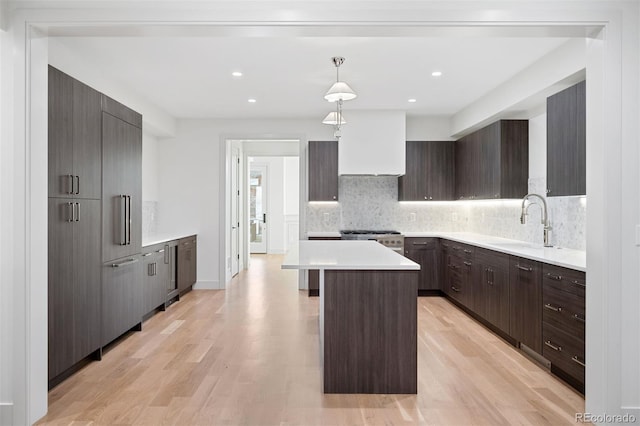 kitchen featuring sink, hanging light fixtures, stainless steel stove, light hardwood / wood-style flooring, and a kitchen island