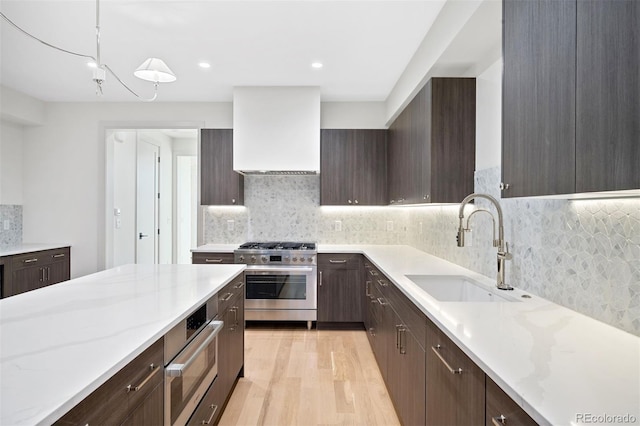 kitchen with appliances with stainless steel finishes, premium range hood, sink, pendant lighting, and light hardwood / wood-style floors