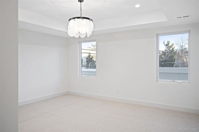 carpeted empty room featuring a tray ceiling and a notable chandelier