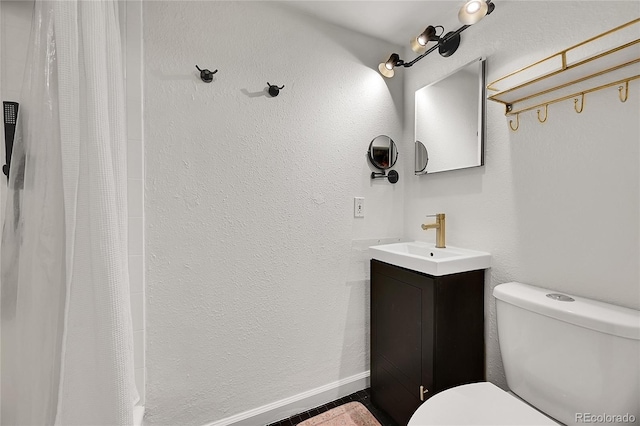 bathroom featuring baseboards, toilet, vanity, and a textured wall