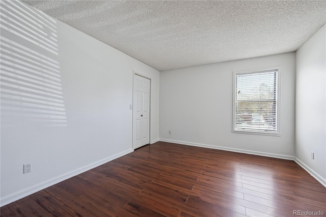 unfurnished room with a textured ceiling, dark wood-style floors, and baseboards