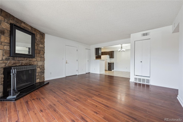 unfurnished living room with wood-type flooring, a chandelier, visible vents, and a fireplace