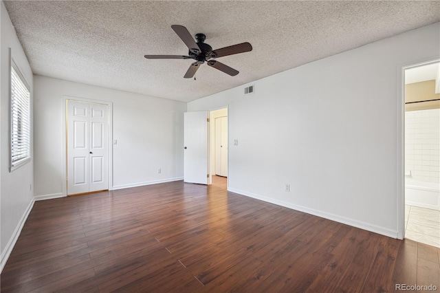 unfurnished bedroom featuring visible vents, baseboards, dark wood-style floors, a textured ceiling, and ensuite bath