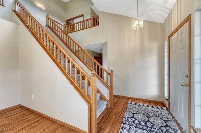 entryway featuring high vaulted ceiling, an inviting chandelier, wood finished floors, and baseboards