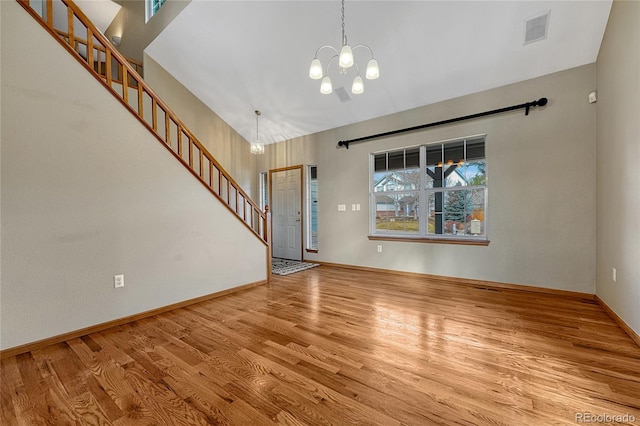 unfurnished living room with visible vents, an inviting chandelier, wood finished floors, baseboards, and stairs