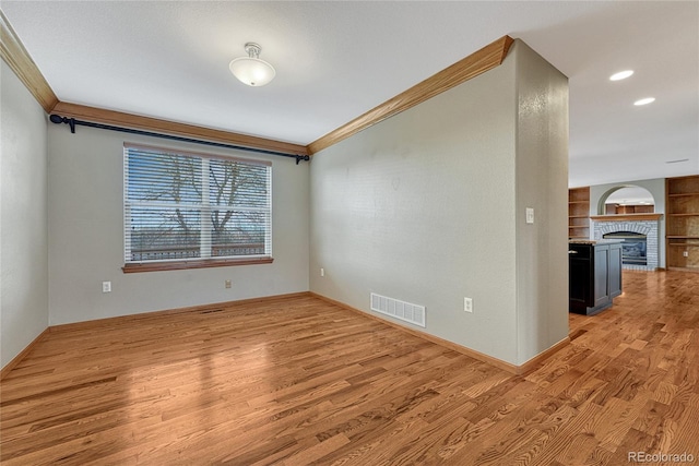 empty room with ornamental molding, a brick fireplace, visible vents, and light wood-style floors