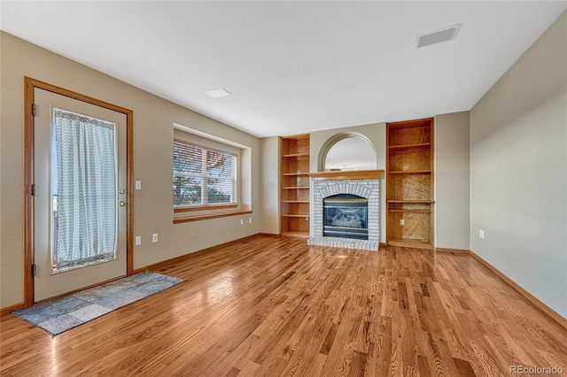 unfurnished living room with built in features, a fireplace, visible vents, light wood-type flooring, and baseboards