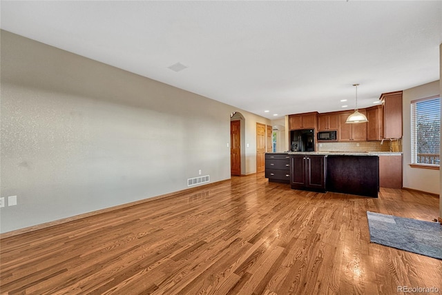 kitchen featuring visible vents, arched walkways, light wood-style floors, a kitchen island, and black appliances