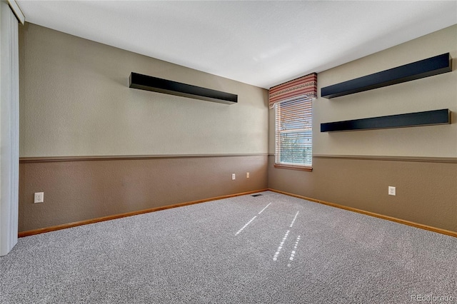 carpeted spare room featuring visible vents, a textured wall, and baseboards