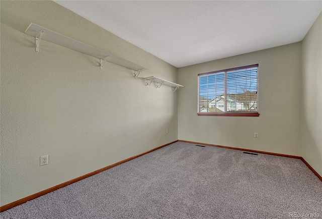 carpeted empty room featuring attic access, visible vents, a textured ceiling, and baseboards