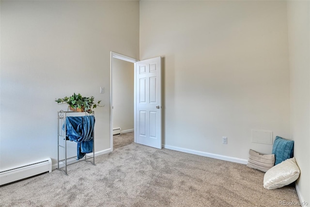 spare room with light colored carpet, a high ceiling, and a baseboard heating unit