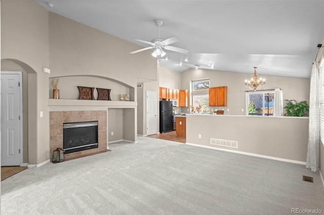 unfurnished living room featuring ceiling fan with notable chandelier, light colored carpet, a fireplace, and vaulted ceiling