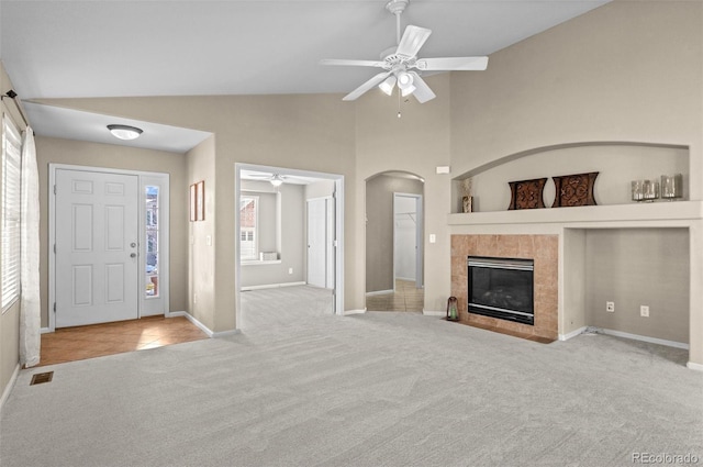 unfurnished living room with high vaulted ceiling, ceiling fan, light carpet, and a tile fireplace