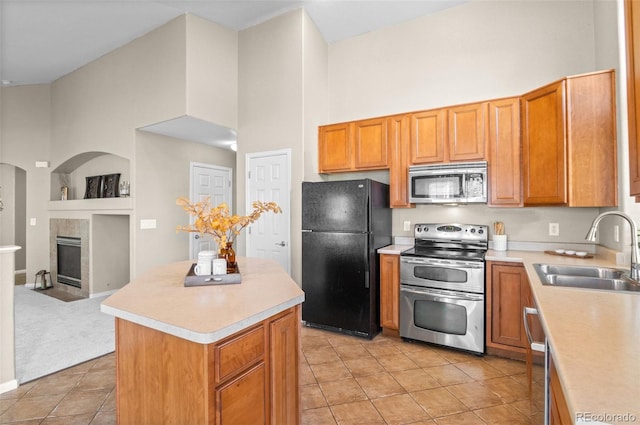 kitchen featuring a high ceiling, sink, a fireplace, appliances with stainless steel finishes, and a kitchen island