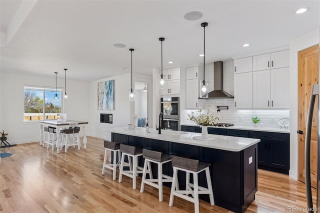 740 W County Road 10e, Berthoud, CO 80513 - kitchen with light wood-type flooring, stainless steel double oven, wall chimney exhaust hood, white cabinets, and tasteful backsplash